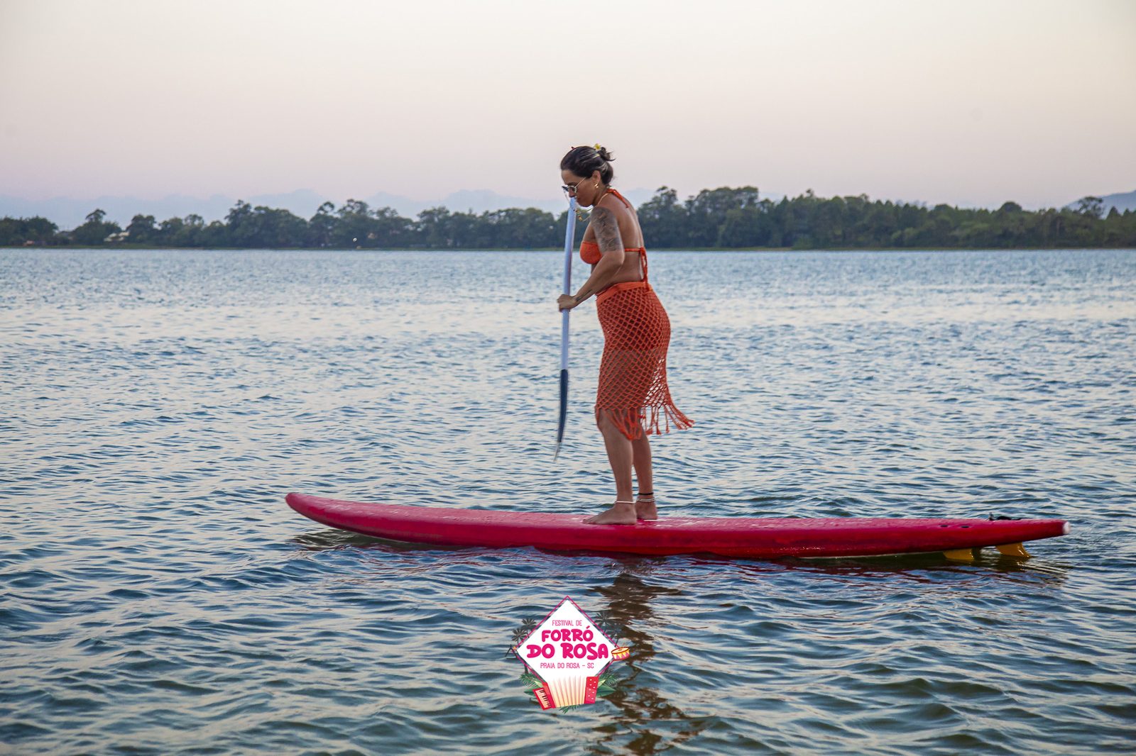 Mulher em pé numa prancha de stand-up paddle na lagoa ao entardecer